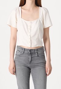 Top corto bianco a maniche corte con scollo quadrato e chiusura a bottoni sul davanti; abbinato a jeans in denim grigio a vita alta.