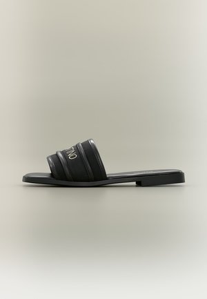 Sandale plate noire à bride large avec trois brides rembourrées sur le dessus du pied et un petit talon, présentée sur un fond neutre.