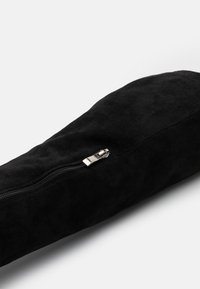 Bolso cilíndrico de ante negro con textura suave y una cremallera plateada. El bolso tiene un diseño elegante y sin adornos.