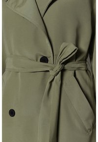 Trench coat verde oliva con cintura ceñida, con cuello muesca y dos botones negros para cierre. Textura de tela suave.