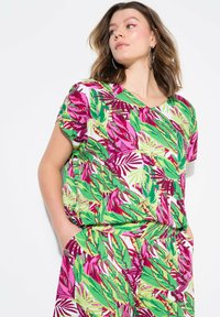 Top a maniche corte caratterizzato da un vivace motivo floreale in verde, rosa e bianco. Il tessuto ha una texture liscia con scollatura a V e una vestibilità ampia.