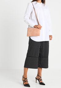 Różowa skórzana torba na ramię o prostokątnym kształcie. Biała koszula zapinana na guziki i czarne, szerokie spodnie w paski. Czarne buty na wysokim obcasie.