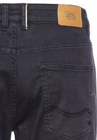 Donkerblauwe denim broek met een getextureerd oppervlak, voorzien van een tan leren logo patch en een achterzak met gestikte details.