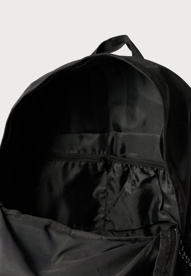 Mochila negra con cierre de cremallera, interior espacioso y un pequeño bolsillo con cremallera en el interior. Fabricada con material de nylon resistente y textura suave.