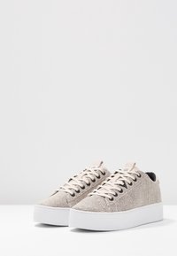 Baskets beiges texturées avec une semelle plateforme blanche lisse, dotées de lacets plats et d'une languette à l'arrière pour un enfilage facile.