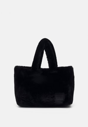 Sac à main rectangulaire en peluche noire avec poignées rembourrées et patch de marque discret en bas à droite sur le devant.