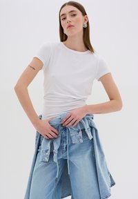 White short-sleeve t-shirt with a smooth texture, paired with loose light blue jeans, and a denim jacket tied at the waist. Silver earrings visible.