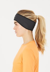 Svart huvudband med vita prickar, tillverkat av ett elastiskt tyg med en slät yta, kombinerat med en orange långärmad topp, hästsvans synlig.