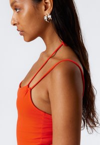 Top rosso senza maniche con spalline sottili, design aderente e una texture liscia. Orecchini a cerchio argentati con un dettaglio intrecciato completano il look.
