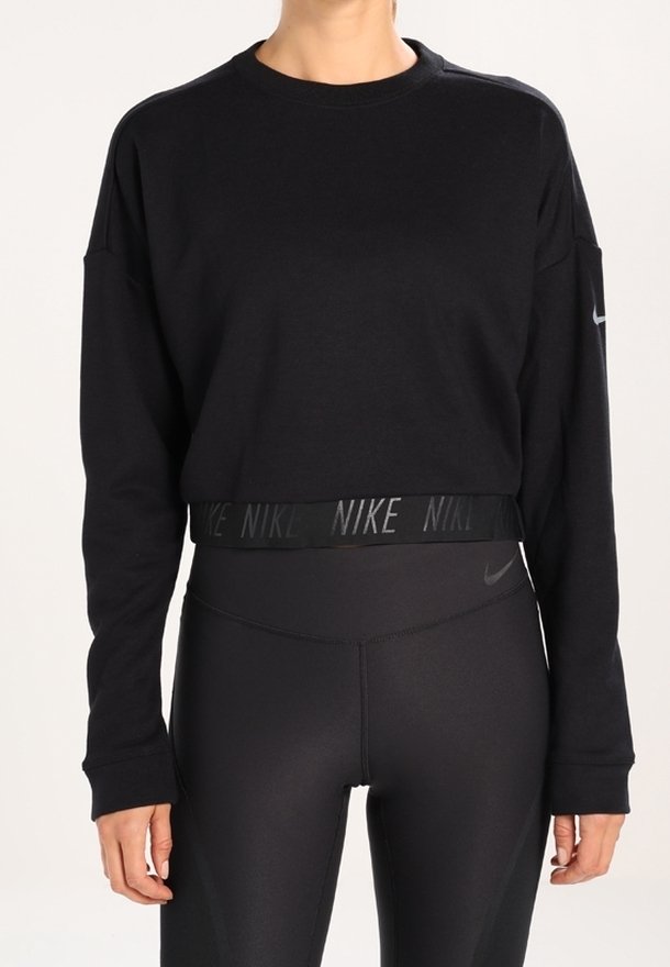 Femme portant un crop top noir à manches longues et des leggings noirs taille haute, tous deux avec des logos Nike subtils.