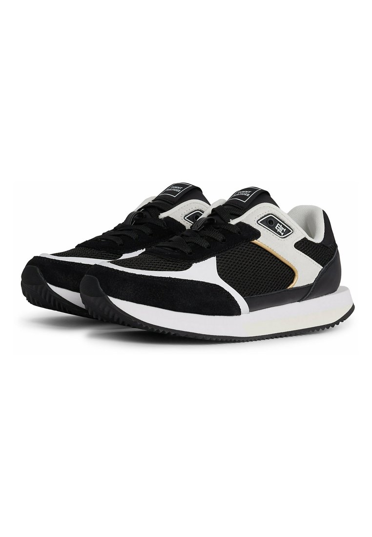 Zapatillas deportivas en blanco y negro con parte superior de malla, acentos de ante, suela de goma y detalles metálicos en el costado.
