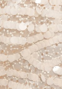 Tissu beige clair orné de sequins circulaires translucides chevauchants et d'accents de fil décoratifs, créant une surface texturée et scintillante.