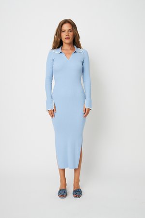 Nő világoskék, bordázott midi ruhában, gyöngy díszítéssel a galléron és a mandzsettán, kék virágos bebújós magas sarkú cipőben.