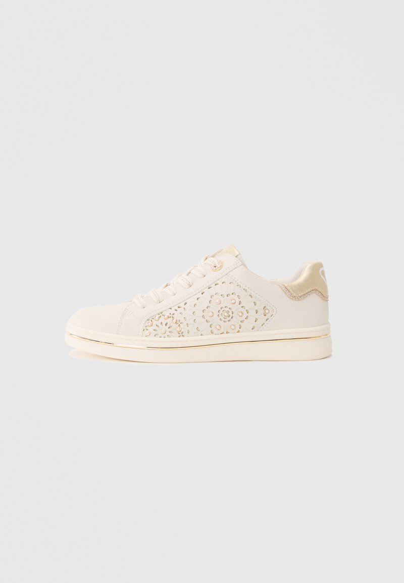 Baskets beiges en toile avec un design floral perforé sur le côté, des accents dorés au niveau du talon et de la semelle, et un système de laçage plat.