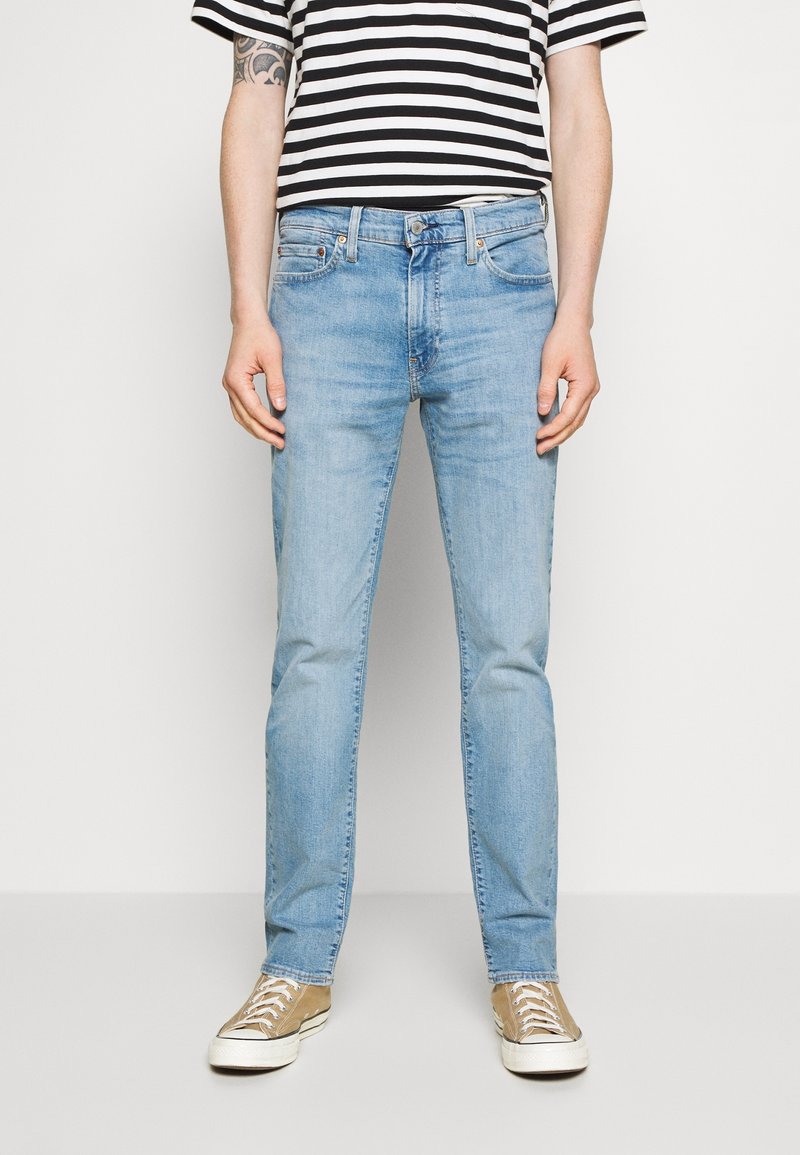 Vaaleansiniset farkut, joissa on slim fit -leikkaus, klassinen viiden taskun muotoilu ja hieman haalistunut pinta. Yhdistetty mustan ja valkoisen raidallisen paidan kanssa.