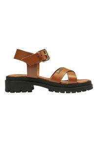 Brune lædersandal med ankelrem og guldbuckle, udstyret med krydset remme og en kraftig sort gummisål med mønster.