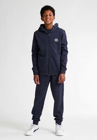 Sudadera con capucha y cremallera en azul marino con pantalones deportivos a juego. Hechos de un tejido suave, cuentan con puños acanalados y un pequeño detalle de logotipo en el pecho.