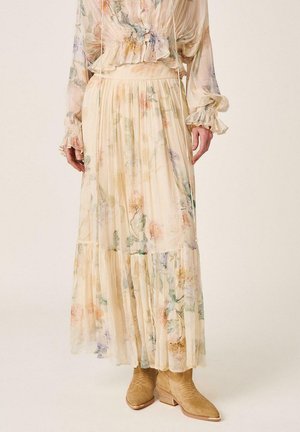 Blusa transparente de manga larga con estampado floral y falda maxi plisada a juego, combinadas con botines beige de ante con tacones de madera.