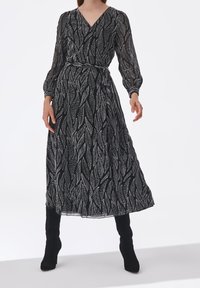 Vestido largo negro con un patrón de hojas, que cuenta con mangas abullonadas largas, escote en V y cintura anudada, fabricado en una tela ligera.