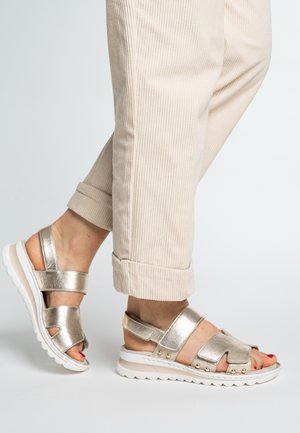 Metallic gold sandals with wide straps, textured finish, and white rubber sole featuring rounded edges and small gold accents.
