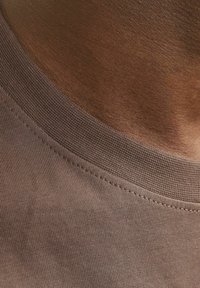 Braunes Baumwoll-T-Shirt-Material mit einem rippenförmigen Rundhalsausschnitt. Die Textur ist glatt, und die Nähte entlang des Ausschnitts sind gleichmäßig und ordentlich.