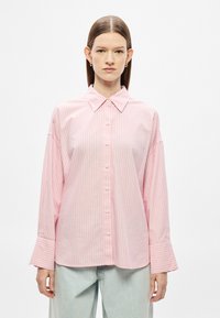 Camisa rosa claro com botões e riscas brancas verticais, apresentando uma gola aberta e punhos abertos. Feita de tecido suave, corte descontraído.