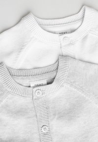 Deux cardigans en maille pliés en blanc et gris clair avec un col rond et des boutons à l'avant.