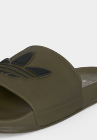 Αθλητική σαγιονάρα Adidas σε ελαιί πράσινο με μαύρο λογότυπο trefoil σε ευρύ λουράκι, υφασμένο πάτο και ελαφρώς ανυψωμένη σόλα.