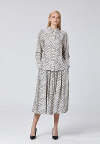 Ensemble composé d'une blouse à boutons et d'une jupe longue en tissu léger avec un motif ondulé noir sur fond crème ; associé à des escarpins noirs.