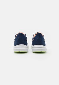 Zapatillas deportivas navy con parte superior de malla texturizada, mediasuela blanca y suela verde. Los acentos naranjas en el talón y el cuello añaden contraste.