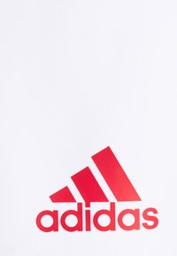Weißer Stoff mit glatter Textur, der ein großes rotes Adidas-Logo zeigt, einschließlich drei schräg verlaufenden Streifen und bolden Kleinbuchstaben.