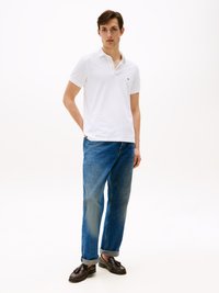 Hvid polo-shirt med korte ærmer og krave, parret med lyseblå tapered jeans og mørke loafers. Enkel, afslappet påklædning.