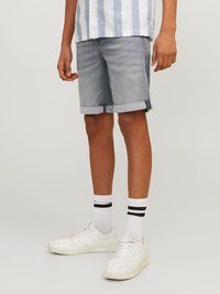 Shorts en denim bleu clair, avec un ourlet retroussé, associés à des baskets blanches et des chaussettes à rayures noires, sous une chemise à rayures à boutons.