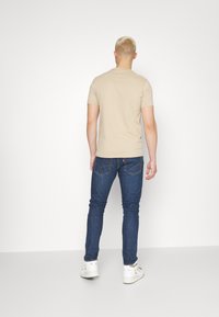 Béžové tričko s krátkým rukávem ve spojení s tmavě modrými džínami. Model má krátké světlé vlasy a bílé tenisky. Jednoduchý a přiléhavý design.