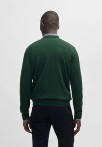 Grön stickad tröja med en figurnära passform, ribbade ärmmuddar och en platt krage, med en kontrasterande grå detalj vid den inre kragen.