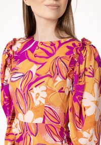 Robe fleurie dans des nuances d'orange et de rose, présentant un design à manches volantes, de grands motifs floraux et une finition en tissu texturé.