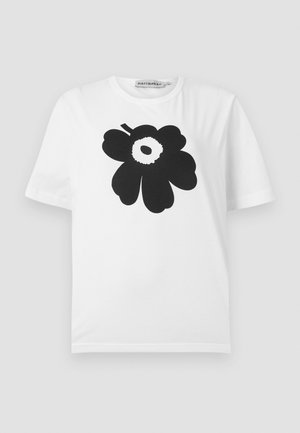 Camiseta de algodón blanca con un diseño floral negro que presenta pétalos redondeados y un punto central, de manga corta y cuello redondo.