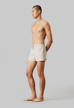 Pantaloni da bagno beige con vita elasticizzata e coulisse, di lunghezza corta, realizzati in materiale leggero, design minimalista, senza motivi visibili.