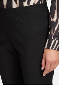 Czarne dopasowane spodnie wykonane z gładkiego materiału, z przednimi kieszeniami i subtelnym czarnym akcentem logo powyżej prawej kieszeni.