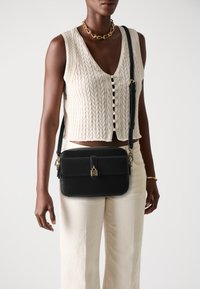 Melna ādas crossbody soma ar zelta aksesuāriem, taisnstūra forma, minimālisma dizains, ar priekšējo atloku un regulējamu siksnu.