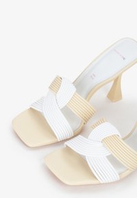 Infradito intrecciati con una combinazione di colori bianco e beige, punta quadrata e tacco angolato di mediana altezza. Realizzati con materiali lisci e dettagli a righe.