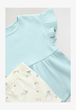 Svjetloplavi rebrasti kratki rukav majica s volanima na rubu u kombinaciji s kremastim kratkim hlačama koje imaju cvjetni uzorak i mrežasti dizajn.