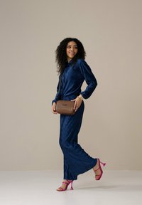 Marineblaues, plissiertes Kleid mit langen Ärmeln, kombiniert mit einer braunen Umhängetasche und rosa High-Heels. Glatte Textur und fließendes Design.