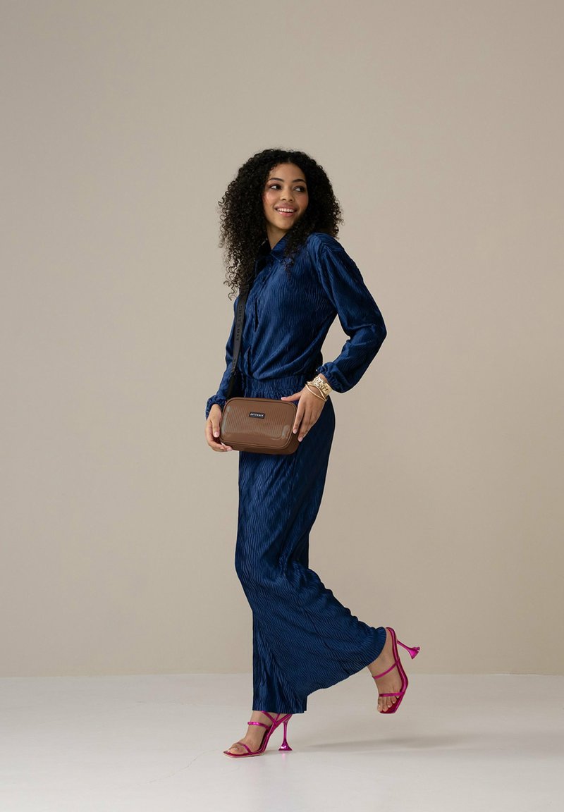 Marineblaues, plissiertes Kleid mit langen Ärmeln, kombiniert mit einer braunen Umhängetasche und rosa High-Heels. Glatte Textur und fließendes Design.