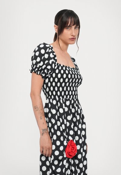 Rochie alb-negru cu buline, cu bust smockat, mâneci bufante și o detaliu dintr-o trandafir roșu din material la talie, fabricată dintr-un material ușor.