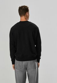 Fekete pulóver, puha anyagból készült, kerek nyakkivágással és bordázott mandzsettákkal, világosszürke farmerral, hátoldali zsebekkel párosítva.