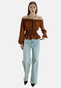 Braunes Off-Shoulder-Oberteil mit gerafftem Taillenbereich und Peplum-Saum, kombiniert mit hellblauen High-Waist-Jeans und schwarzen spitzen Heels.