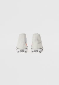 Hellegraue High-Top-Canvas-Sneaker mit Gummisohle, schwarzen Streifen und runder Logoplatte an der äußeren Ferse.