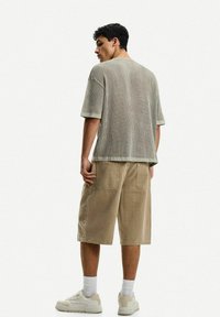 Gray ribbed short-sleeve shirt paired with khaki knee-length shorts. White sneakers with textured design. Model viewed from the back.