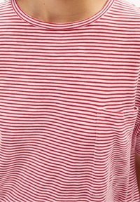 Czerwono-biała koszulka w paski z okrągłym dekoltem i małą kieszonką po lewej stronie. Wykonana z bawełnianego materiału o miękkiej fakturze.